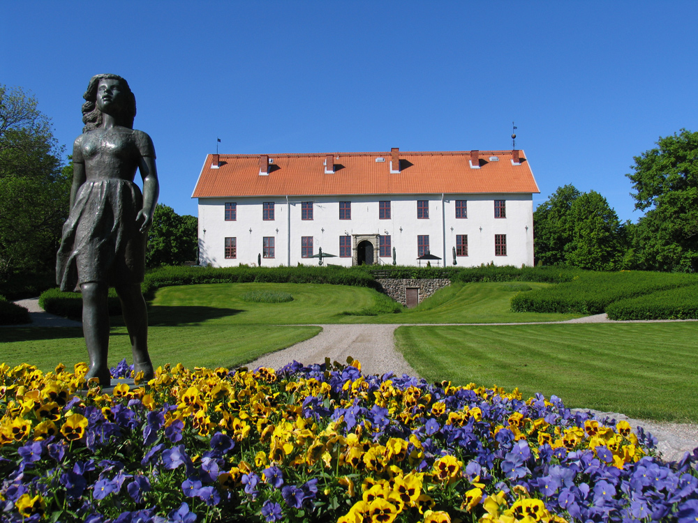 En staty vid en blomsterrabatt med Sundbyholms Slott i bakgrunden.